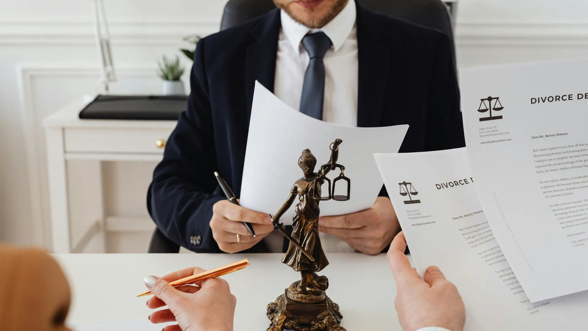 A man in a suit and tie sitting at a table with a statue of justice.